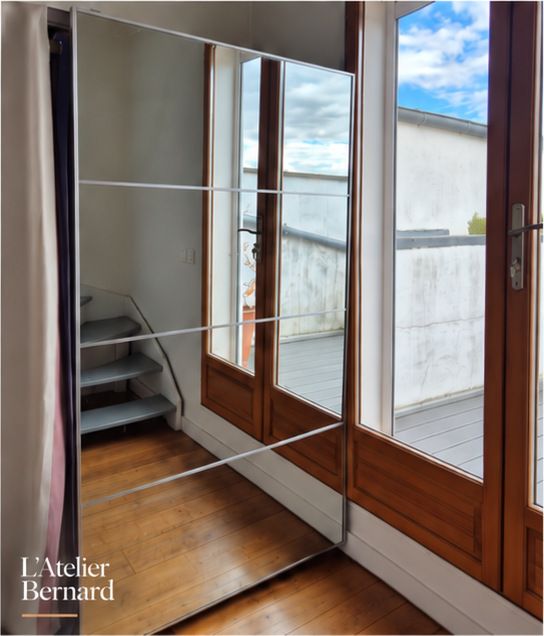 Grand miroir à côté d’une porte-fenêtre en bois, sur un parquet, avec une terrasse au fond