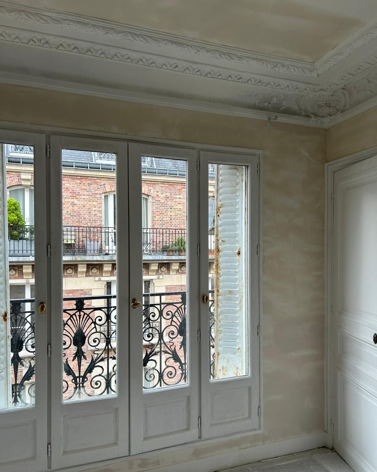 Portes-fenêtres blanches avec garde-corps en fer forgé, moulures au plafond et murs enduits dans un appartement en travaux
