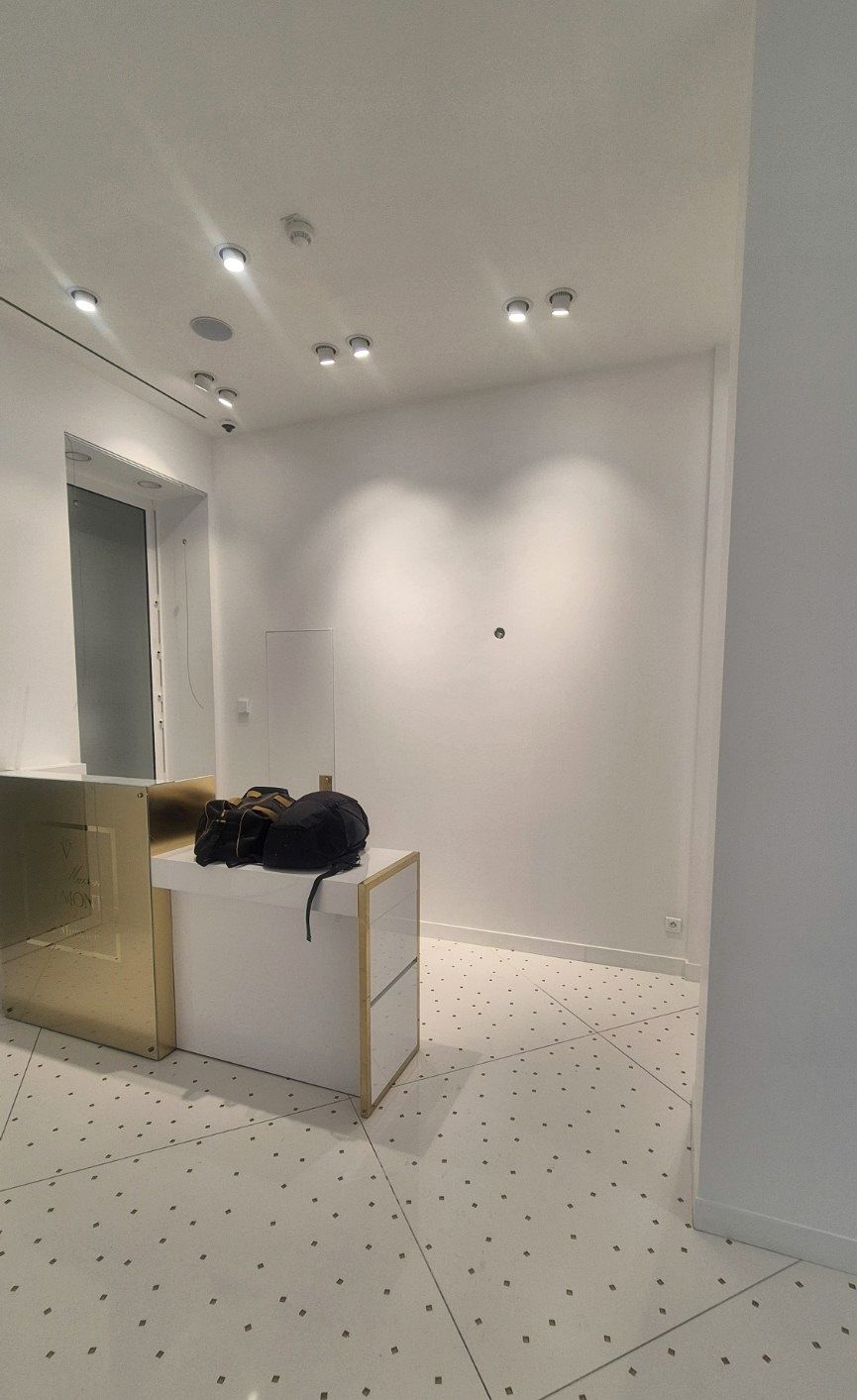 Entrée d’une boutique parisienne remise en état : murs blancs, spots au plafond, comptoir et sol clair à motifs