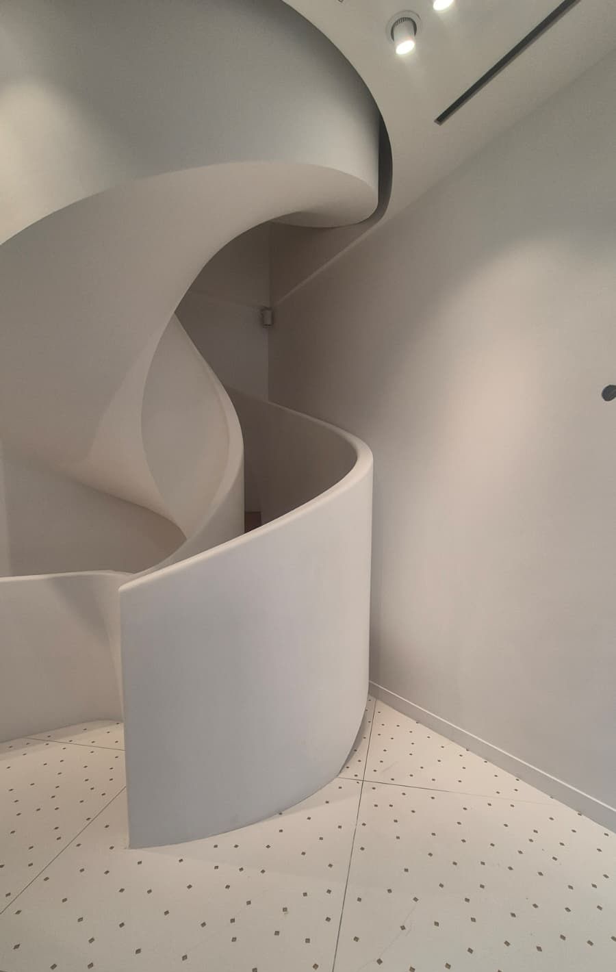 Escalier hélicoïdal blanc d’une boutique parisienne, murs blancs et sol clair semé de petits points sombres