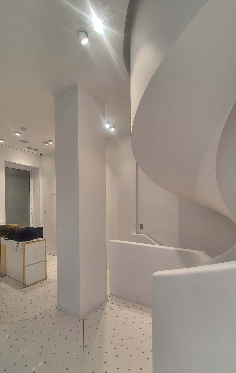 Boutique blanche à Paris avec un pilier, un comptoir et un escalier hélicoïdal blanc, sol clair à motifs
