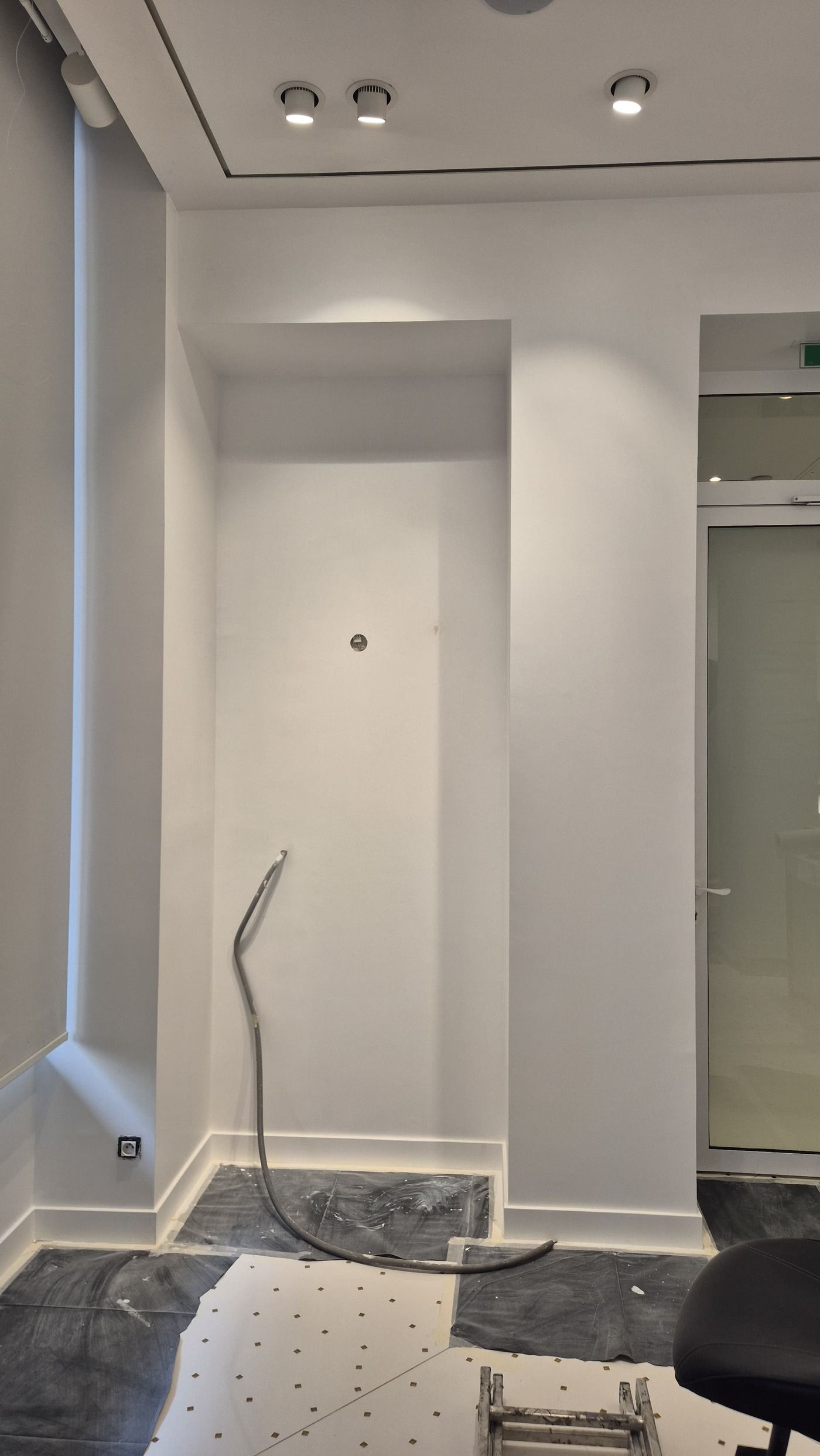 Mur blanc d’une boutique avec une niche, des protections au sol et une gaine, pendant l’intervention