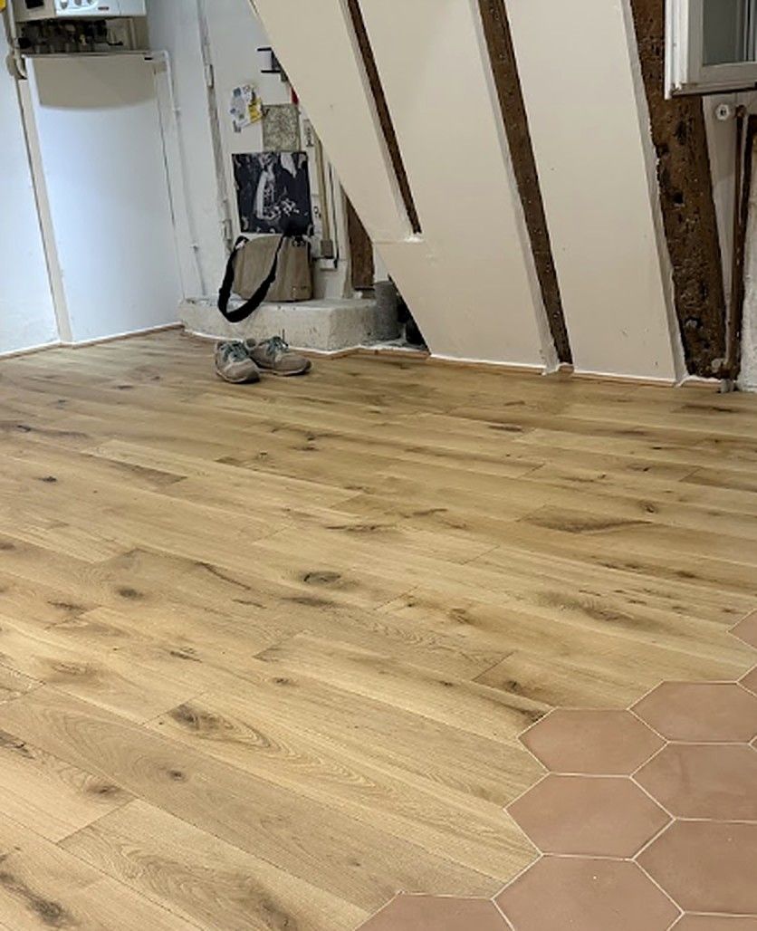 Parquet en chêne posé dans une pièce, avec le carrelage hexagonal qui le rejoint dans l’angle
