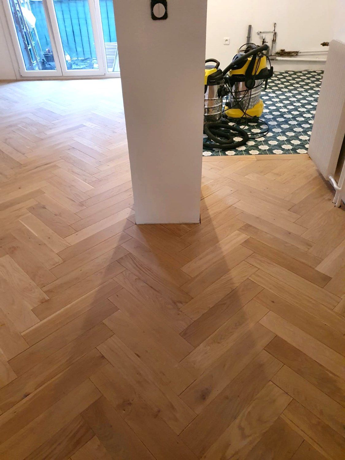 Parquet en chevrons posé autour d’un pilier, avec un sol en carreaux décorés dans la pièce voisine