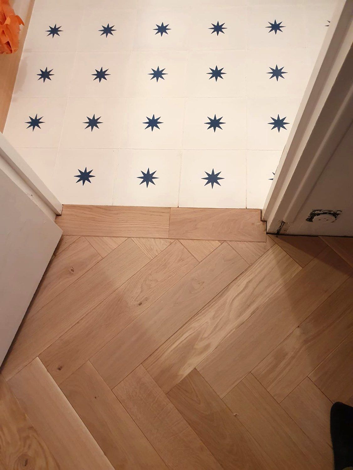 Détail de finition entre des carreaux blancs à étoiles bleues et un parquet en chevrons, au niveau d’un seuil