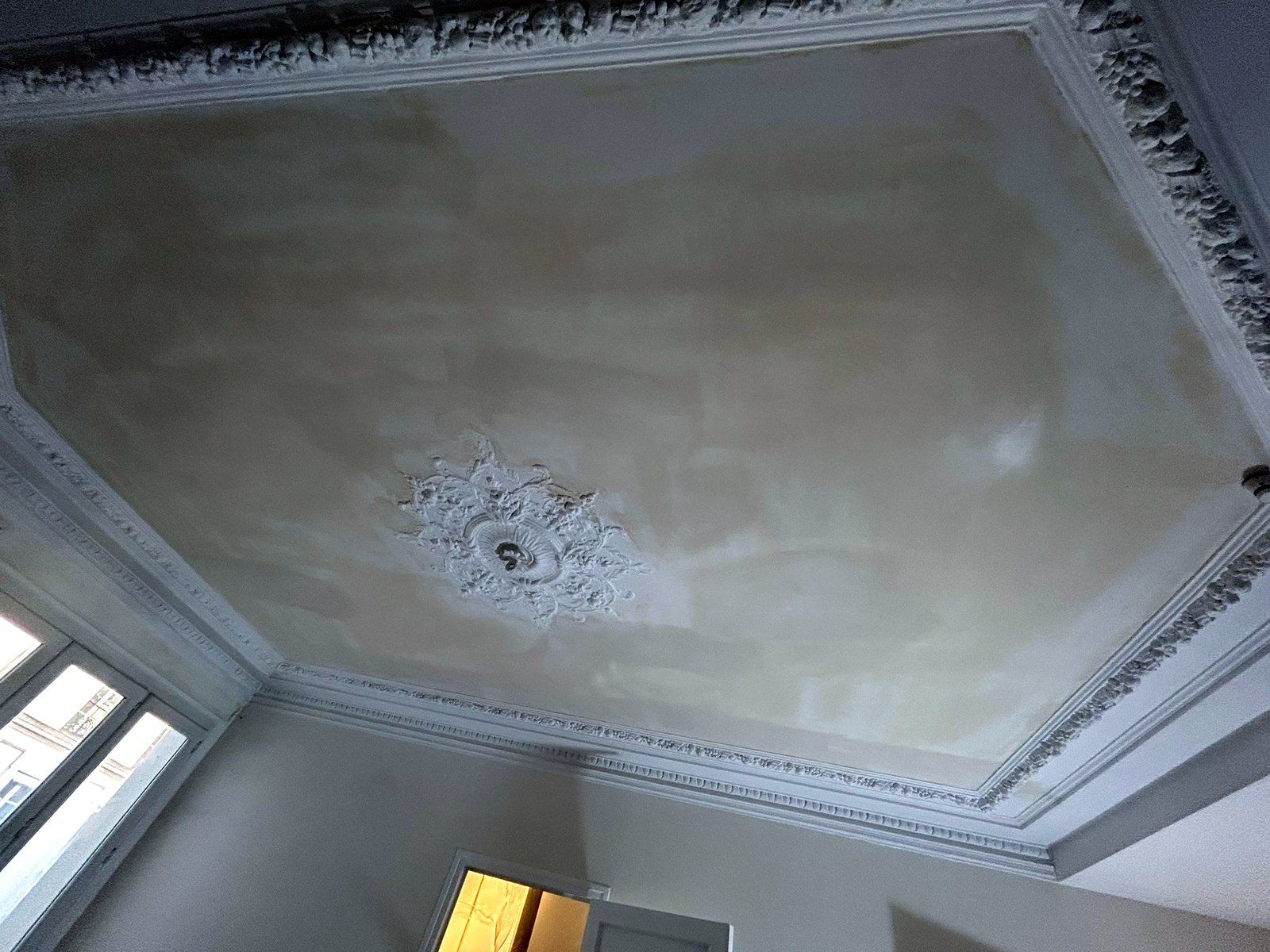 Plafond d’un appartement parisien avec corniche et rosace en plâtre, zones reprises à l’enduit