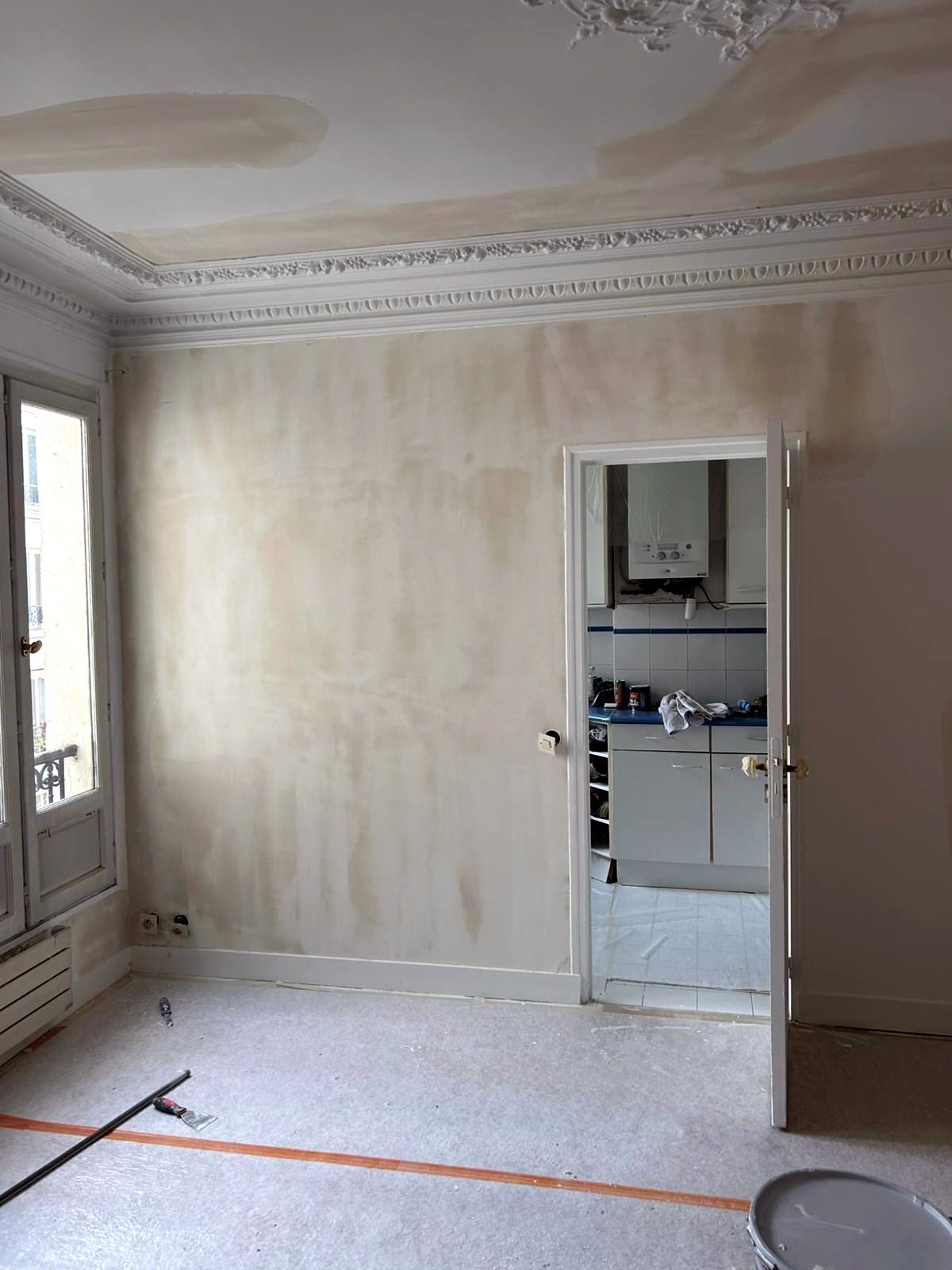 Pièce d’un appartement parisien en remise en état : murs repris à l’enduit, plafond à corniche et rosace, sol protégé par un film