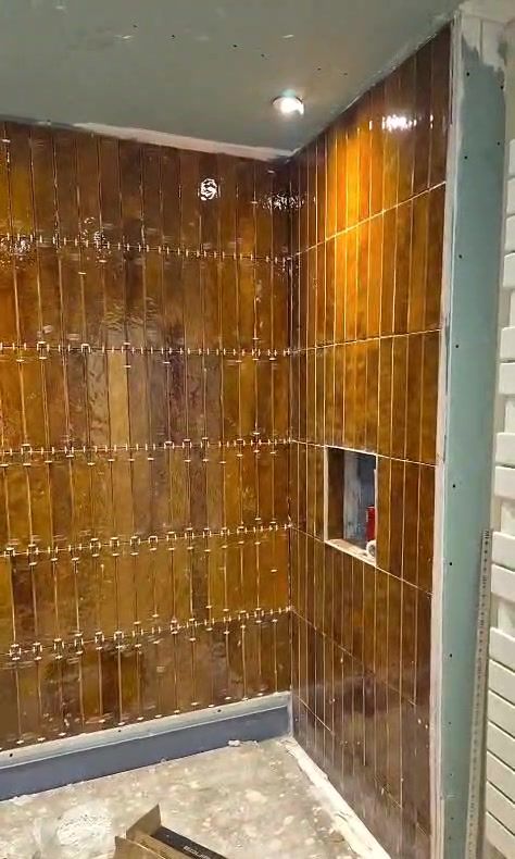 Mur de douche en cours de carrelage : carreaux émaillés ambrés posés à la verticale, niche intégrée