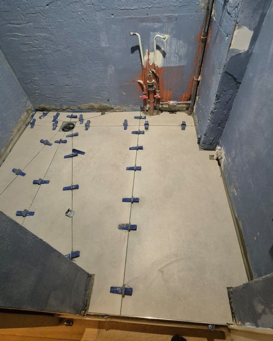 Sol d’une salle d’eau en cours de pose : grands carreaux calés par des croisillons bleus, bonde et arrivées d’eau en attente