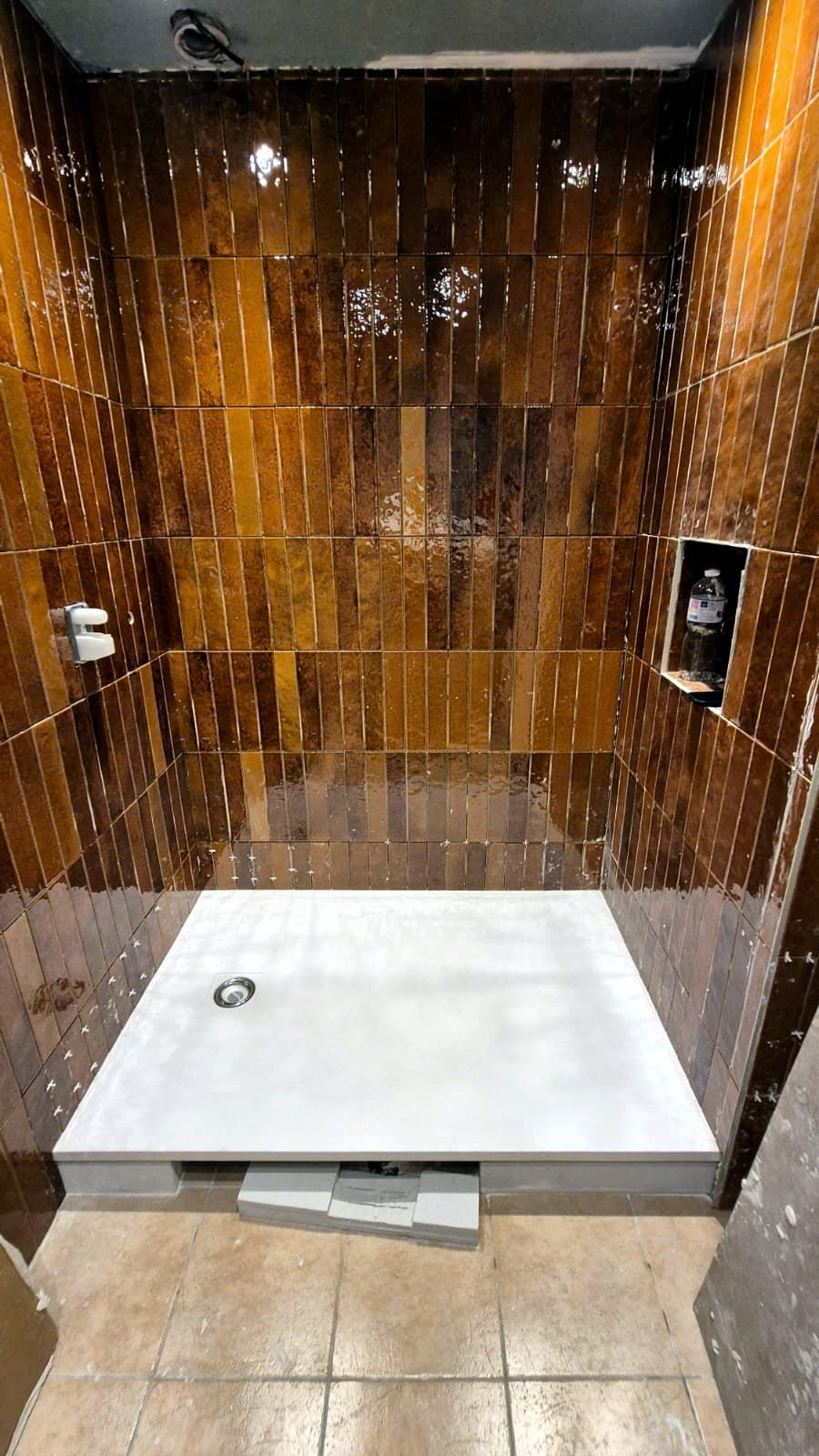 Douche en cours de finition : murs en carreaux émaillés ambrés posés à la verticale, niche intégrée, receveur blanc avec bonde posé sur le sol carrelé