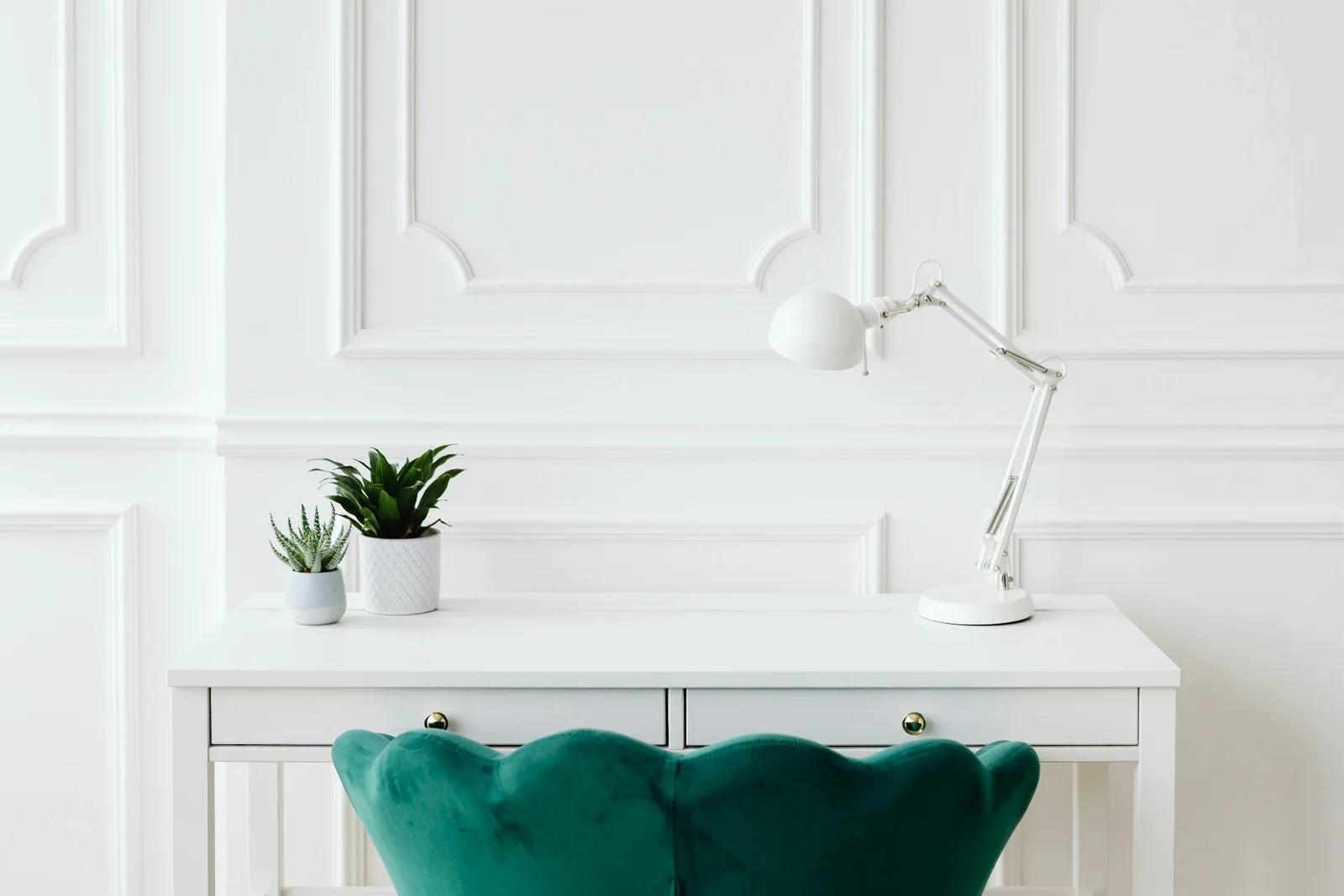 Bureau blanc devant un mur à boiseries, avec une lampe articulée et un fauteuil en velours vert
