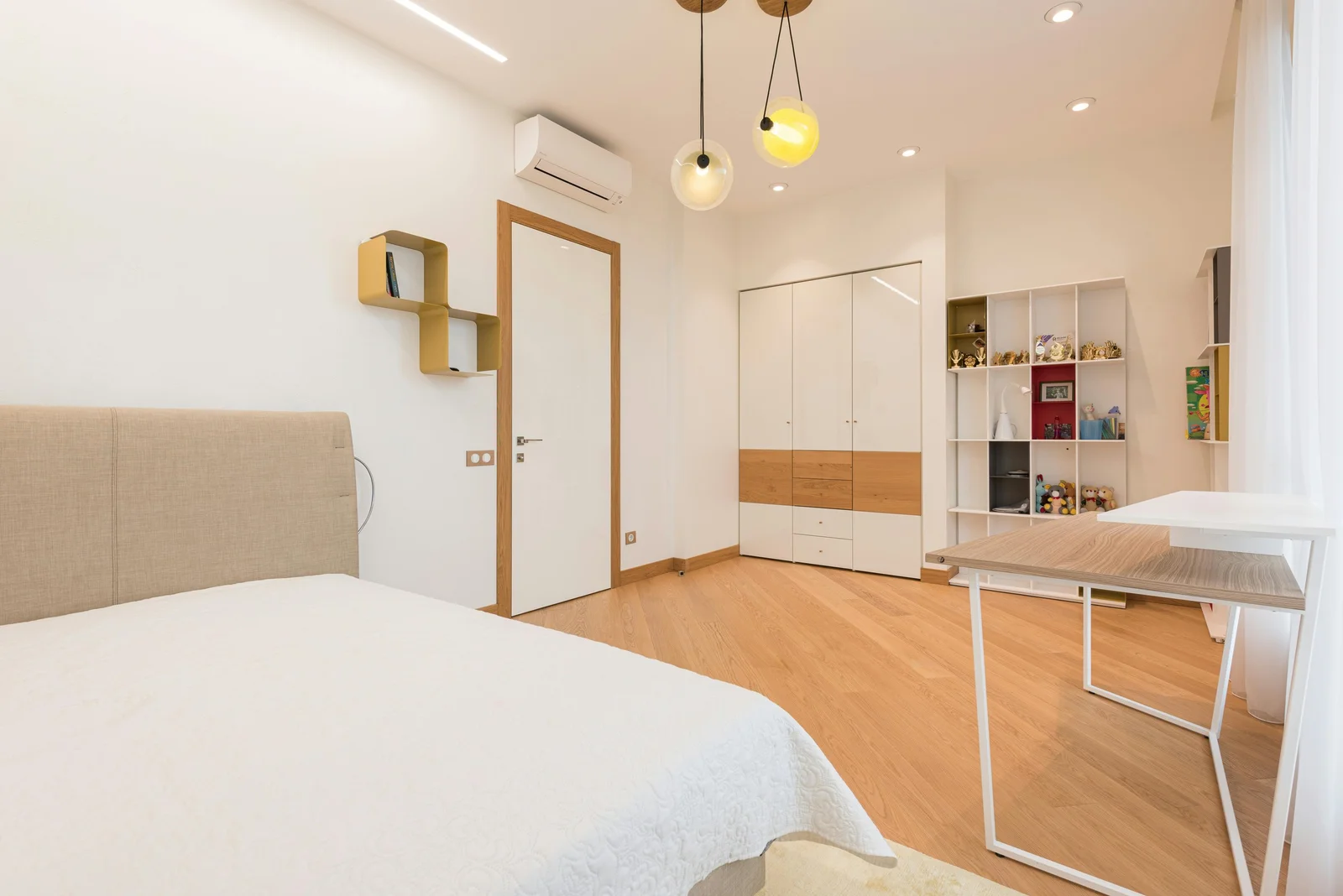 Chambre claire avec parquet, une grande armoire blanche à touches de bois, des étagères cubes et un bureau
