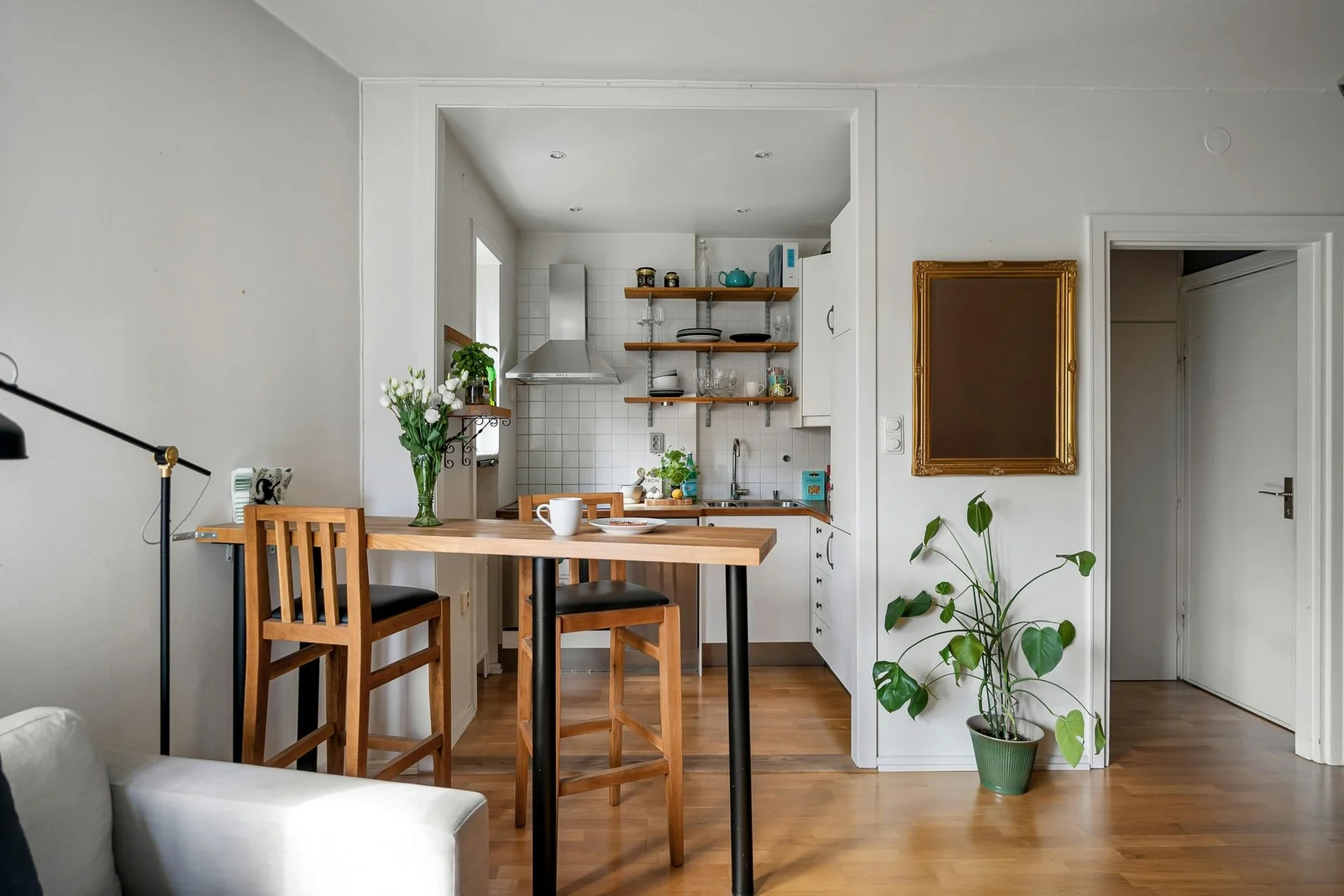 Pièce de vie avec cuisine ouverte en arrière-plan, étagères en bois, grande table en bois avec chaises et parquet