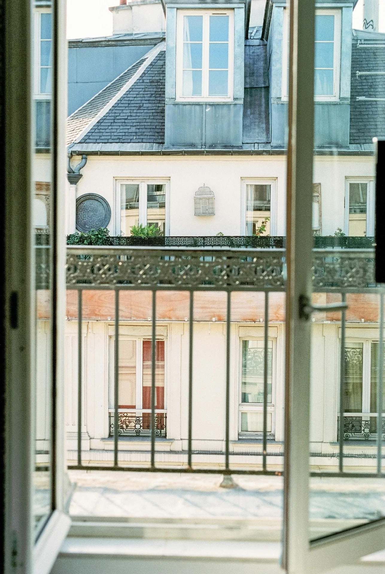Fenêtre ouverte sur un balcon en fer forgé et des immeubles aux toits en zinc