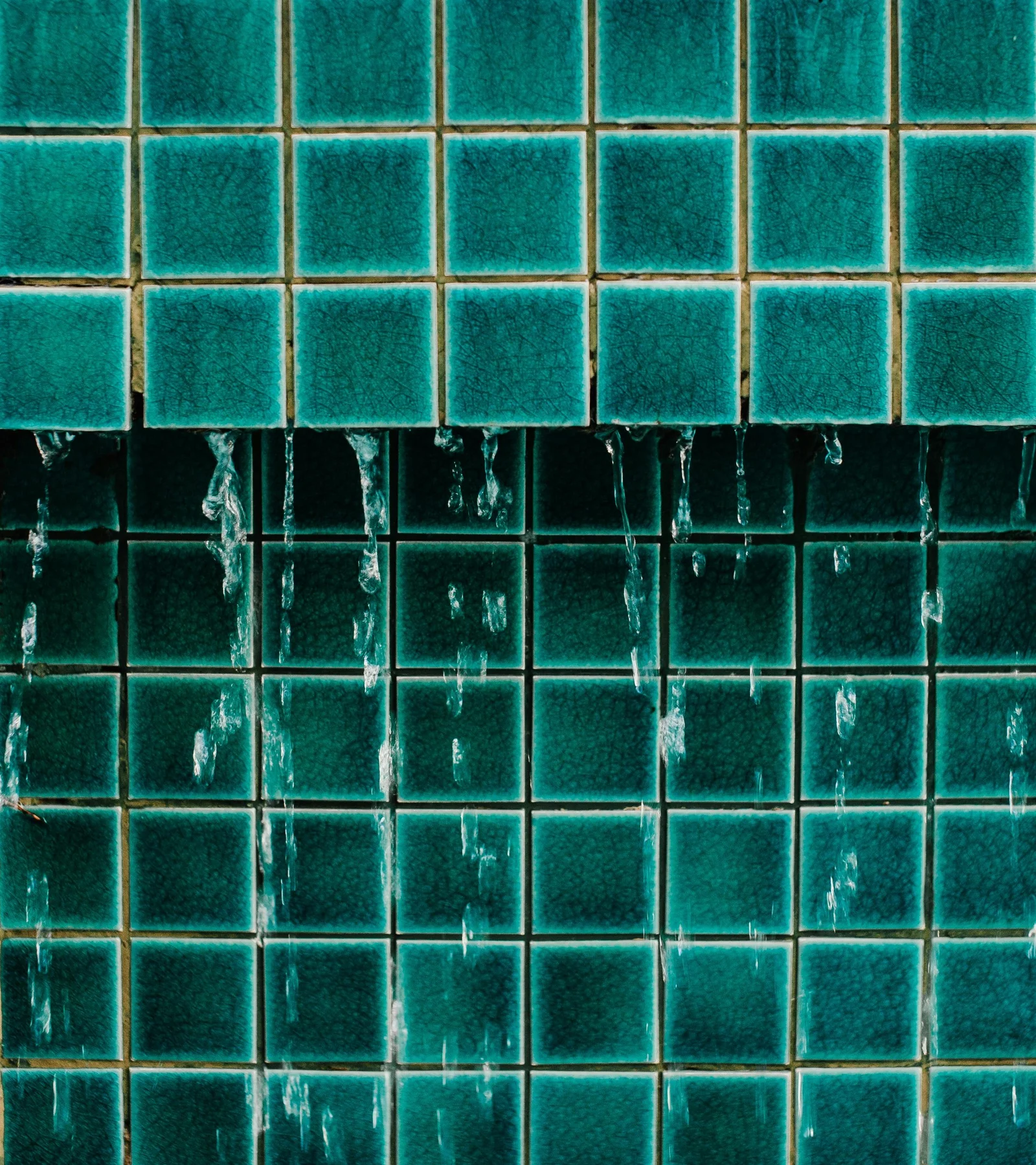 Mosaïque de petits carreaux émaillés turquoise, avec de l’eau qui ruisselle sur la partie basse