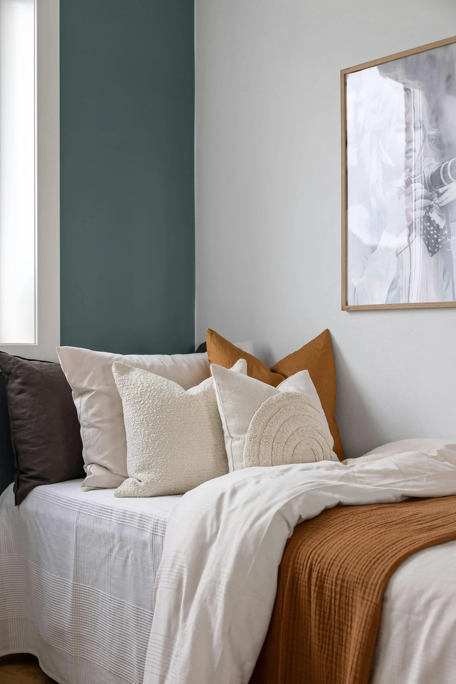 Chambre avec un pan de mur bleu-vert ardoise derrière un lit garni de coussins beiges et d’un plaid terracotta