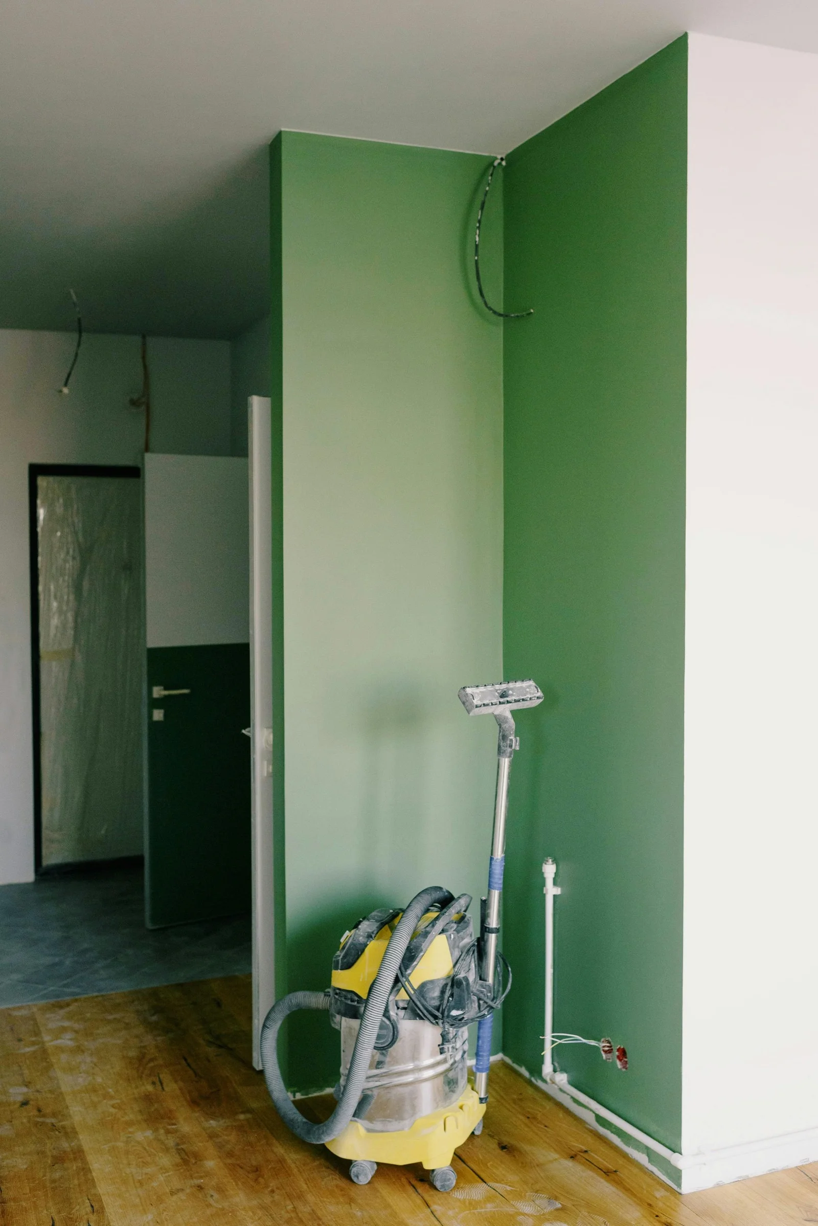 Mur d’angle peint en deux tons de vert au-dessus d’un parquet en chêne, dans un couloir avec un aspirateur de chantier