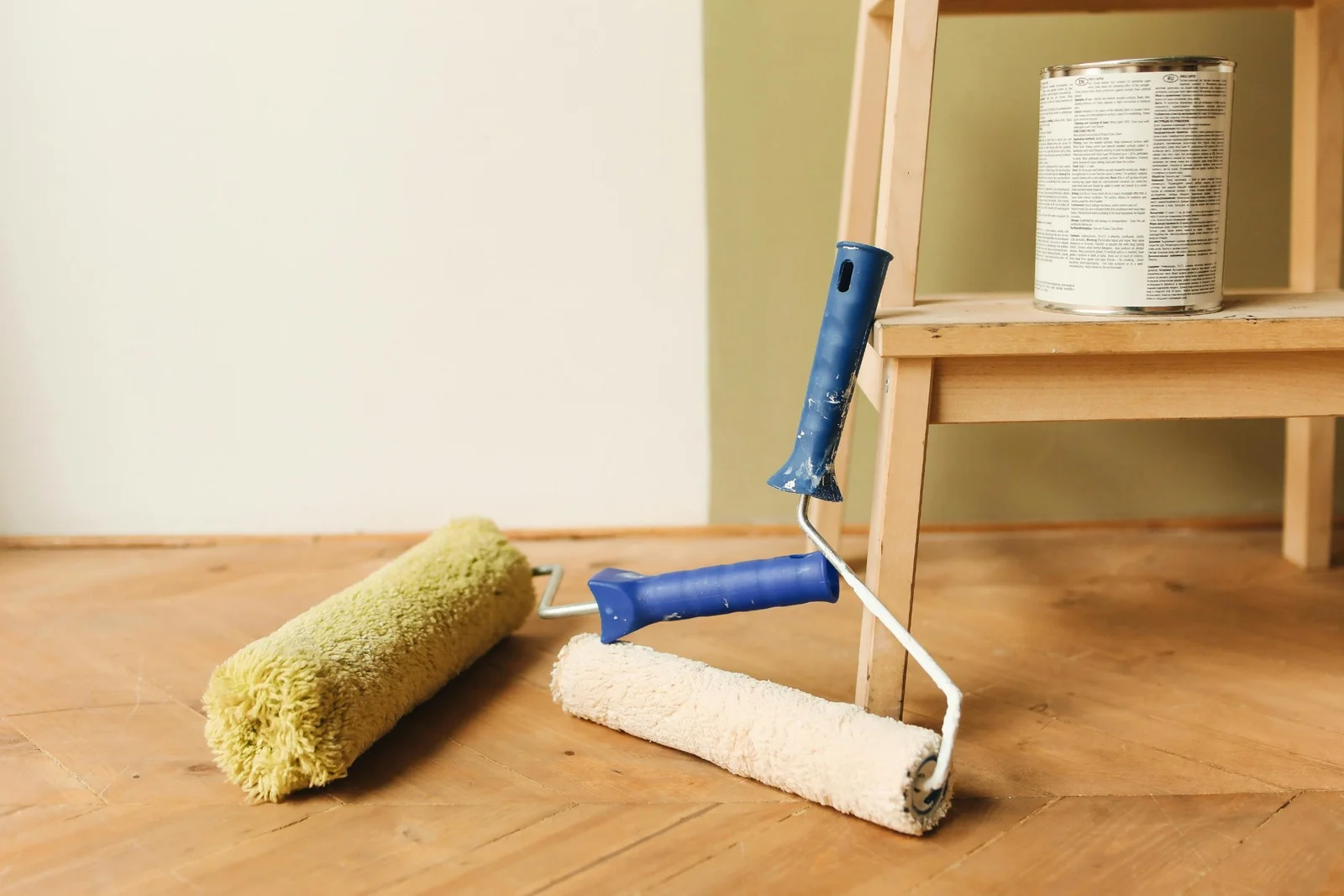 Deux rouleaux de peinture posés sur un parquet, devant un mur vert clair et une échelle en bois