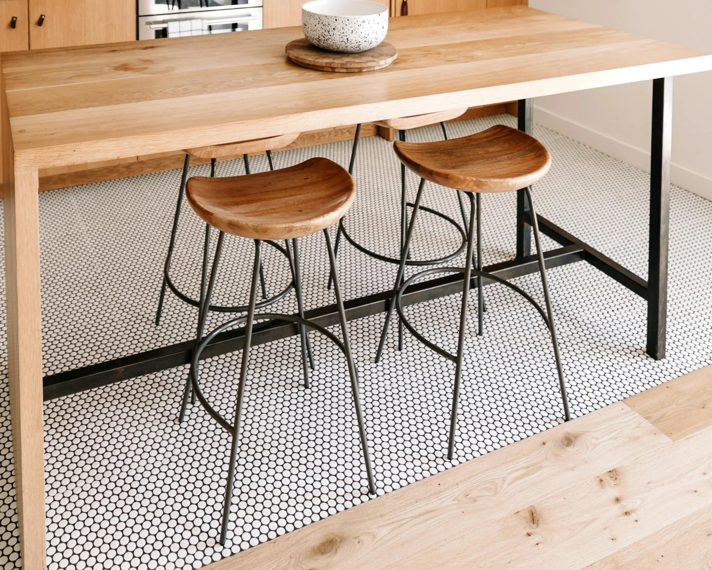 Table haute en chêne massif avec deux tabourets, sur un sol en petits carreaux blancs et noirs qui rejoint un parquet clair